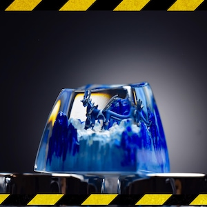 Könnte beinhalten: Ein durchscheinender blau-weißer Resin-Keycap mit einer Drachenfigur im Inneren. Der Keycap hat eine rechteckige Form mit abgerundeten Kanten. Der Drache ist eine detaillierte, blaue Skulptur. Der Hintergrund ist ein Farbverlauf von Dunkel- zu Hellgrau.