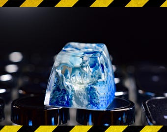 May include: A blue and white resin keycap with a detailed design of a white animal in a snowy landscape.