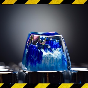 May include: A blue and white resin keycap with a clear top, showing a swirling blue and white design inside. The keycap is sitting on a silver keyboard.