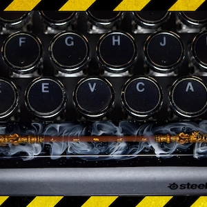 Peut inclure: Un clavier noir et or avec un capuchon de touche personnalisé représentant une baguette magique avec de la fumée blanche. Le clavier a un fond noir et blanc avec le texte "steelseries" en blanc.