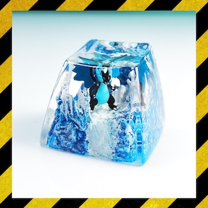 May include: A clear, square resin keycap with a blue and black dragon figure set within a blue and white icy landscape. This keycap is a unique accessory for mechanical keyboards, adding a custom aesthetic.