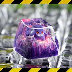 May include: A custom keycap featuring a purple Gengar character with a menacing grin, set within a translucent, crystalline resin. The keycap has a purple and pink color scheme, and is designed for mechanical keyboards.