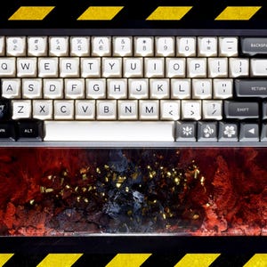 May include: A mechanical keyboard with white keycaps and black and grey accents. The keyboard has a custom wrist rest with a red and gold design. The keys are labelled with letters, numbers, and symbols.