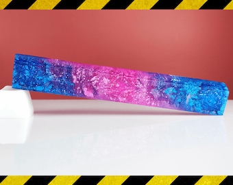 May include: A rectangular, colorful object with a blue and pink marbled design, resting on a white, geometric shape. The background is a solid red color, and the overall aesthetic is modern and artistic.