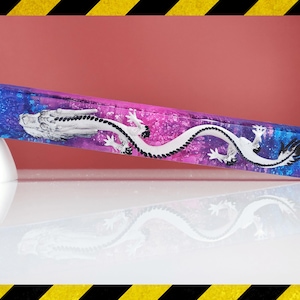 May include: A rectangular, colorful resin object with a dragon design. The object has a gradient of blue, purple, and pink hues. A white dragon is painted on the surface. The object is resting on a white surface.