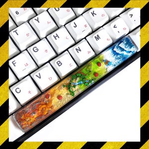 May include: A custom keyboard space bar with a vibrant design. The bar depicts a landscape with fire, grass, and water, and red accents. The keyboard keys are white with Japanese characters.