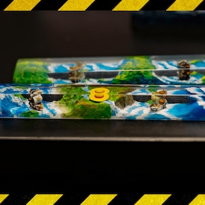 Op de afbeelding: Twee aangepaste toetsenbordtoetsen met een landschapsontwerp. De toetsen hebben een blauwe en witte oceaan met groene eilanden en kleine figuren. Een gele acht staat op één toets.