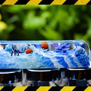 Puede incluir: Una tecla personalizada con una escena oceánica azul y blanca, que incorpora figuras Pokémon en miniatura y Poké Balls. La tecla transparente muestra la escena detallada. Diseñada para un teclado mecánico, añade una estética única.