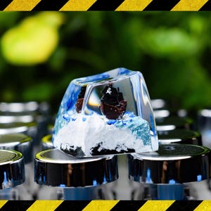 以下が含まれることがあります： ミニチュア海賊船が内包された、透明な長方形のキーキャップ。キーキャップは、海の波と雪のベースを模した青と白のアクセントが特徴です。船は茶色で、黒い旗が付いています。