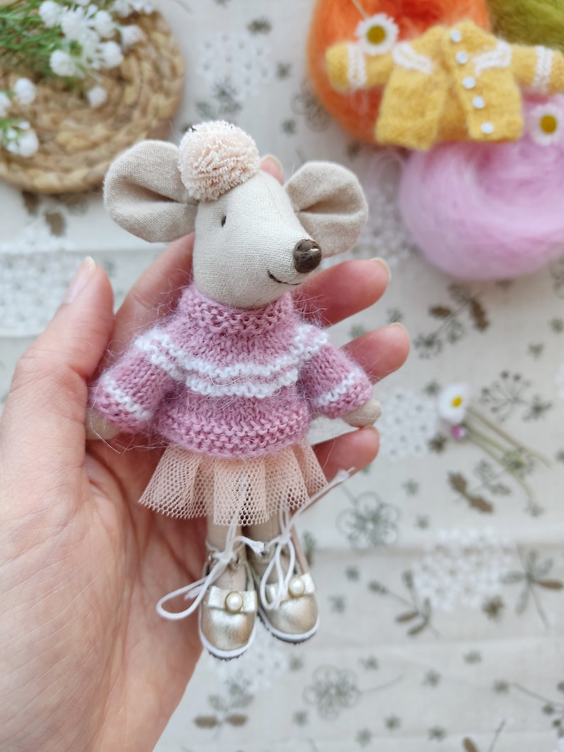 May include: A small, handmade mouse doll wearing a pink and white striped sweater, a tulle skirt, and gold shoes. The doll is being held in a hand.