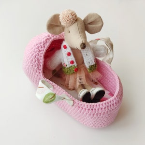May include: A pink crocheted basket with a white and green knitted cardigan and a pink tulle skirt, holding a plush mouse toy with a brown nose and a pink pom-pom on its head.