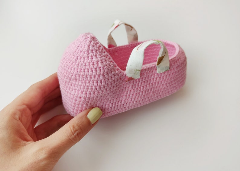 May include: A pink crocheted baby shoe with white fabric straps. The shoe is made with a delicate stitch pattern.