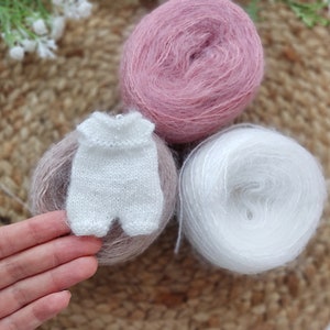 May include: A white knitted baby onesie with a pink and white yarn skein in the background.