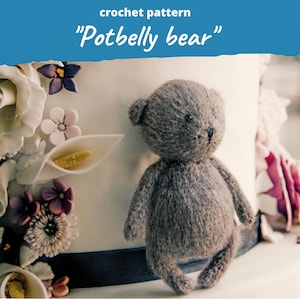 May include: A handmade gray crochet bear with a potbelly, standing in front of a decorated cake. The bear has small black eyes and a dark nose. The text "crochet pattern" and "Potbelly bear" are visible in the image.