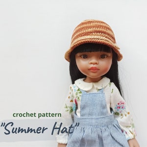 Può includere: Un modello all'uncinetto per un "Cappello estivo" è mostrato su una bambola. Il cappello è a righe marroni e beige. La bambola indossa una camicia con stampa floreale e una salopette a righe blu. Il testo "crochet pattern" e "Summer Hat" sono visibili.