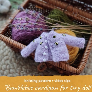 May include: A miniature lavender cardigan with yellow and black bumblebee appliques. The tiny sweater has white buttons and is displayed in a wicker basket with yarn and lavender sprigs. The text on the image reads "Bumblebee cardigan for tiny doll".