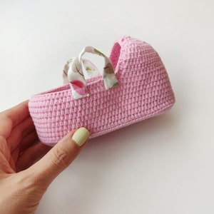 May include: A pink crocheted basket with fabric handles featuring a floral pattern. The basket is small and would be suitable for holding small items.