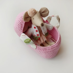 May include: A pink crocheted basket with a fabric handle and a small stuffed mouse wearing a white sweater and a pink skirt inside.