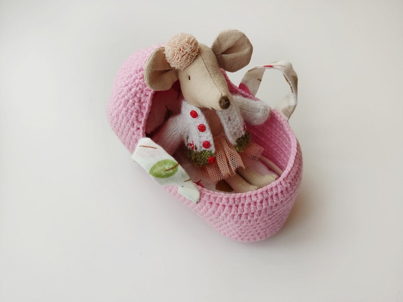May include: A pink crocheted basket with a fabric handle and a small stuffed mouse wearing a white sweater and a pink skirt inside.