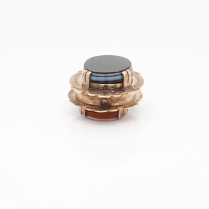 May include: A gold-toned ring with a layered agate stone. The top layer is black, the middle layer is blue and white, and the bottom layer is orange.