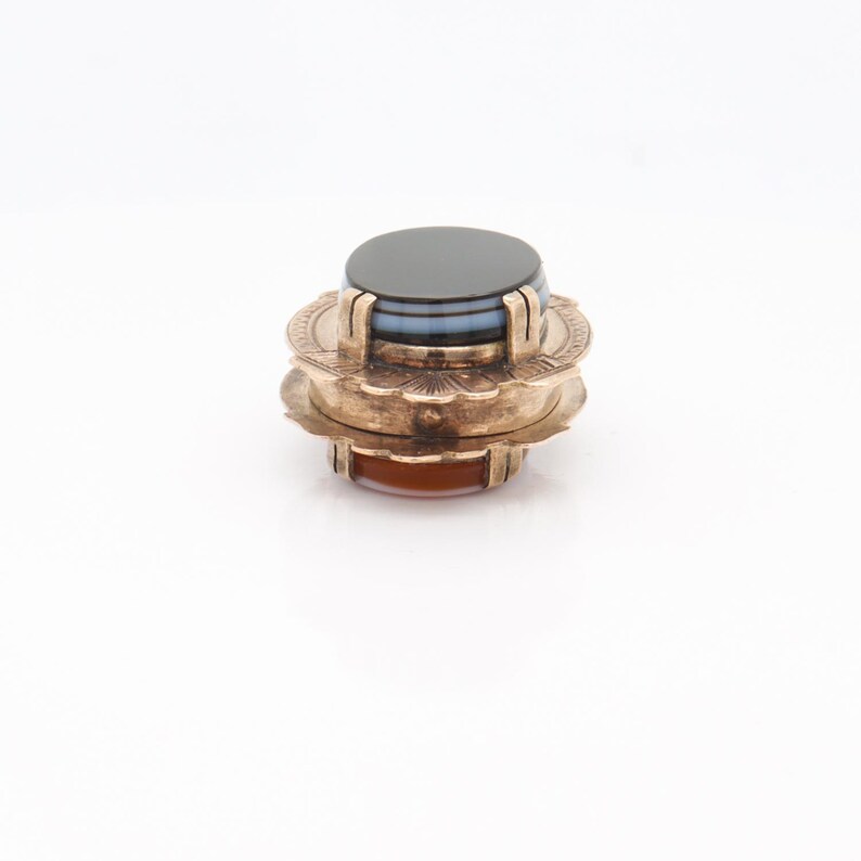 May include: A gold-toned ring with a layered agate stone. The top layer is black, the middle layer is blue and white, and the bottom layer is orange.