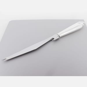 May include: A silver cheese knife with a serrated blade and a forked tip. The handle has a rounded, elegant design. The knife also features a bottle opener. The knife is displayed on a grey surface.