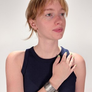 Puede incluir: Un brazalete de plata con un dise&ntilde;o intrincado. El brazalete se lleva en la mu&ntilde;eca izquierda de una persona que lleva una camiseta sin mangas azul oscuro.