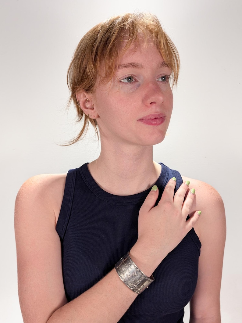 Puede incluir: Un brazalete de plata con un dise&ntilde;o intrincado. El brazalete se lleva en la mu&ntilde;eca izquierda de una persona que lleva una camiseta sin mangas azul oscuro.
