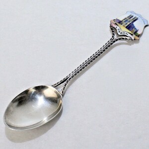 May include: Silver souvenir spoon with a twisted handle and a round bowl. The spoon has a colorful enamel design of a building with the word "LONDON" on it.