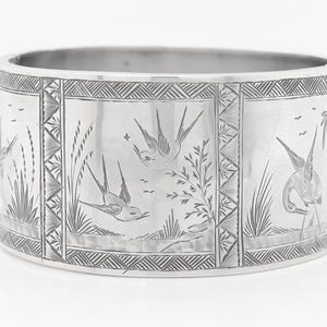 Puede incluir: Pulsera de plata con un dise&ntilde;o grabado de p&aacute;jaros y follaje. La pulsera tiene un patr&oacute;n geom&eacute;trico alrededor del borde.