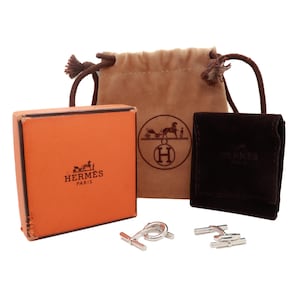 May include: A set of silver cufflinks in the shape of a horse and carriage. The cufflinks are packaged in a brown box with the Hermes logo and come with a brown velvet pouch.