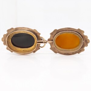 May include: A gold locket pendant with two oval compartments. One compartment has a black background and the other has a yellow background.