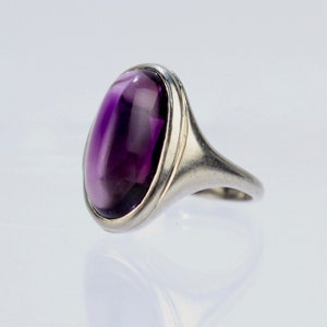 May include: A silver ring featuring a large, oval-shaped amethyst gemstone. The ring has a simple, elegant design.