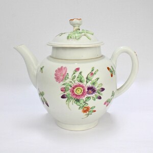 Puede incluir: Tetera de porcelana blanca con un diseño floral. La tetera tiene una tapa con un pomo en la parte superior. Las flores son rosas, moradas y naranjas.