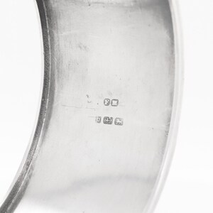 Puede incluir: Primer plano del interior de una pulsera de brazalete de plata con marcas de contraste, incluida la letra "F" y el n&uacute;mero "925".