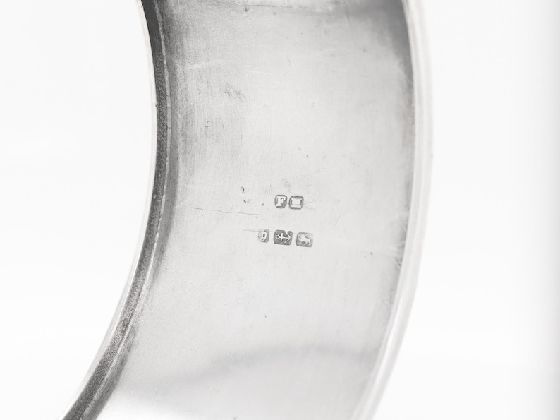 Puede incluir: Primer plano del interior de una pulsera de brazalete de plata con marcas de contraste, incluida la letra "F" y el n&uacute;mero "925".