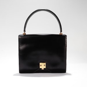 Puede incluir: Un bolso de mano de cuero negro con cierre dorado y asa superior.