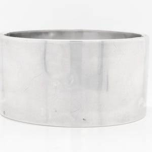 Puede incluir: Un brazalete de plata con un acabado liso y pulido.