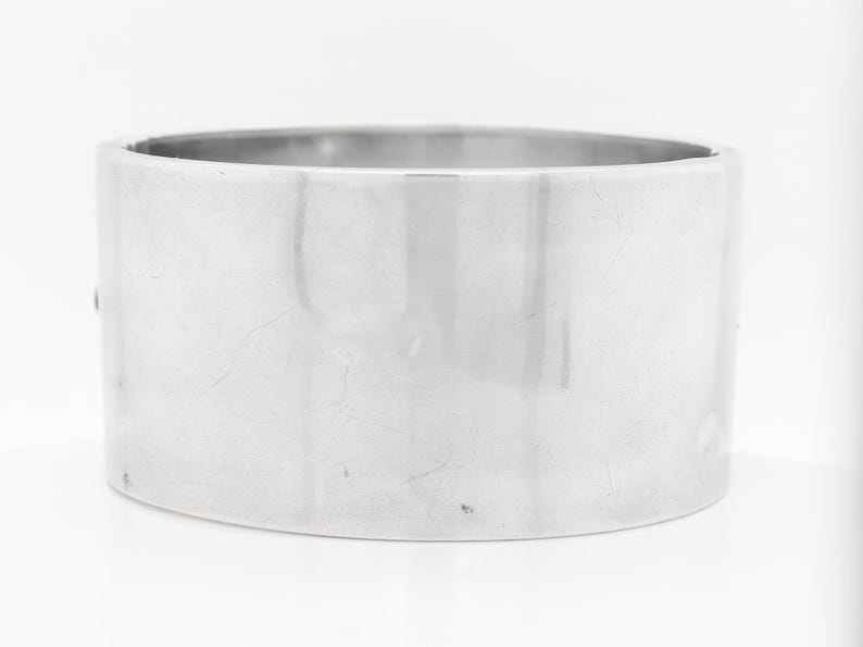 Puede incluir: Un brazalete de plata con un acabado liso y pulido.