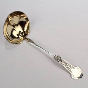Puede incluir: Un cucharón de servir de plata con un mango adornado y un cuenco chapado en oro.