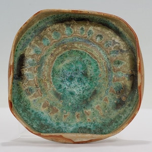 Puede incluir: Un plato cuadrado de cerámica con un esmalte verde y marrón. El plato tiene un borde elevado y un patrón decorativo en el centro.