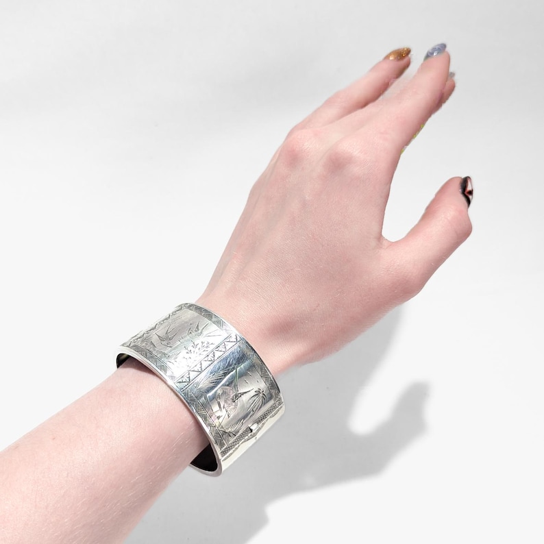 Puede incluir: Un brazalete de plata con un dise&ntilde;o grabado intrincado. El dise&ntilde;o presenta un motivo floral y patrones geom&eacute;tricos.