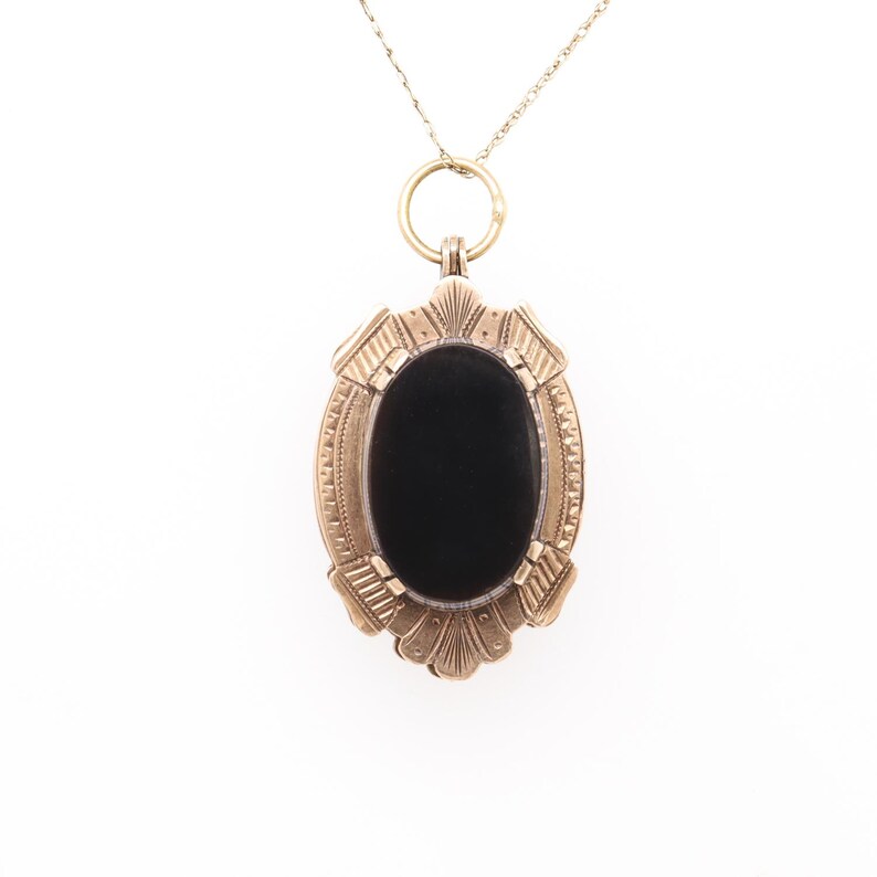 May include: A gold locket pendant with a black oval cameo. The locket has a detailed ornate design around the cameo.
