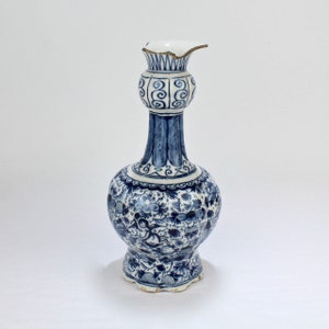 Könnte beinhalten: Eine blaue und weiße Keramikvase mit einem bauchigen Körper und einem schmalen Hals. Die Vase ist mit einem Blumenmuster und einer Szene mit einer Figur in einer Landschaft verziert.