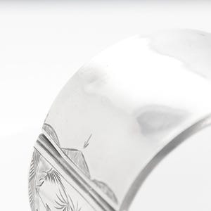 Puede incluir: Un brazalete de plata con un dise&ntilde;o grabado. El brazalete est&aacute; abierto y tiene un cierre con bisagra.