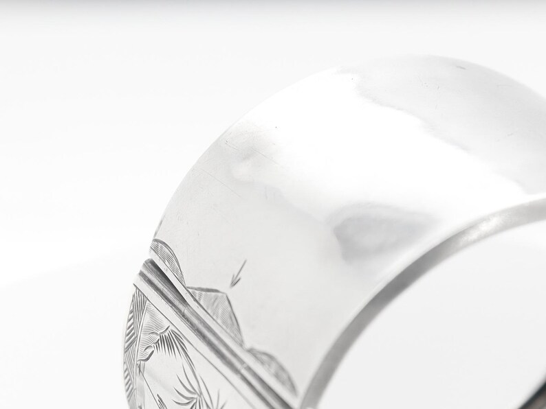 Puede incluir: Un brazalete de plata con un dise&ntilde;o grabado. El brazalete est&aacute; abierto y tiene un cierre con bisagra.