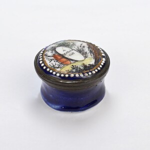 May include: A small, round, blue and white porcelain trinket box with a lid. The lid has a painted scene of a woman and a child in a landscape with the words "A Mother's Gift".