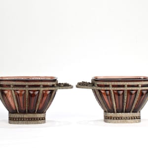 Puede incluir: Dos cuencos decorativos con base de vidrio marrón y detalles en metal plateado. Los cuencos tienen forma rectangular y están decorados con un borde de cuentas.