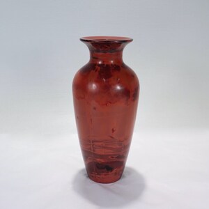 May include: A red ceramic vase with a marbled design. The vase has a wide mouth and a narrow base.