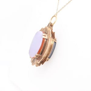 May include: A gold pendant necklace with a cameo featuring a white oval stone surrounded by a red and black stone border. The pendant is attached to a delicate gold chain.